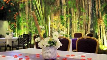 A table with a vase of flowers and red rose petals on a tablecloth.