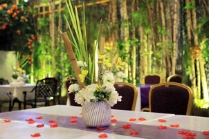 Una mesa con un jarrón de flores y pétalos de rosa roja sobre un mantel.