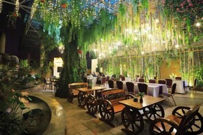 An indoor restaurant with wooden tables and chairs, surrounded by lush greenery and hanging lights. - Yiyang Hotel (Yiling Wanda Plaza, Yichang Three Gorges Enterprise Base) (Yichang)