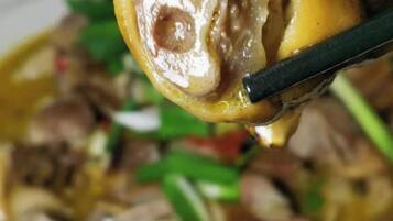 A close-up of a dish with a piece of meat and a vegetable, possibly a stir-fry, being held by chopsticks.