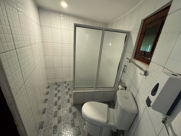 A bathroom with a toilet, a glass-enclosed shower, tiled walls, and a window with a wooden frame.