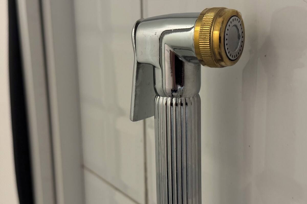 Un grifo cromado con pomo dorado, sujeto a una pared de azulejos blancos.