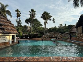 A pool area with a stone bridge, palm trees, and a sign indicating 'DEEP END'.