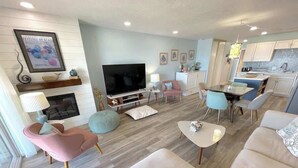 Un saló modern amb televisió, places per seure, una llar de foc i una zona de cuina.