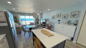 Una cuina moderna amb una illa gran, zona de menjador amb cadires i vista a l'oceà.