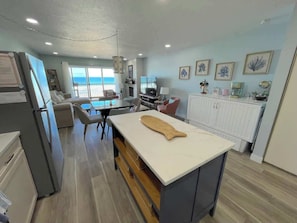 A modern kitchen with a large island, dining area with chairs, and a view of the ocean.