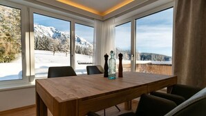 En matplats med ett träbord och stolar, stora fönster med utsikt över ett snötäckt berg och två saltströare på bordet.
