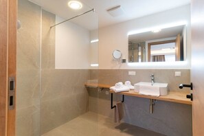 A modern bathroom with a glass-enclosed shower, a wooden vanity with a sink, and a mirror above the mirror. - Waldrand Apartments (Ramsau am Dachstein)