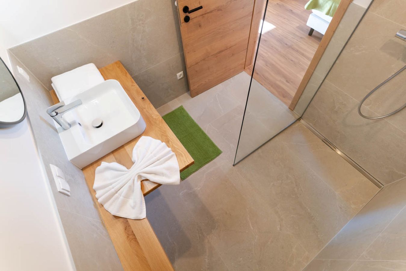 A modern bathroom with a white sink, wooden vanity, and a green rug.