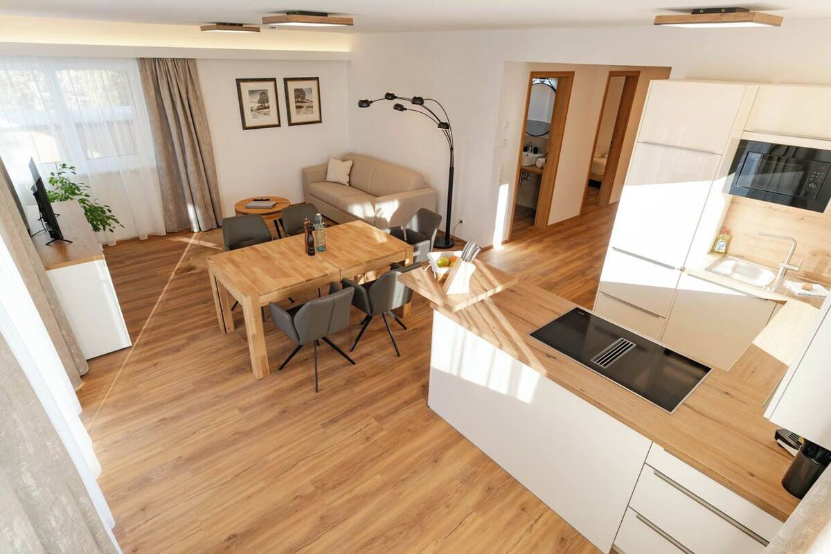Une cuisine moderne dotée d’un plan de travail en bois, d’un four encastré et d’un évier. On y trouve également un coin repas avec une table et des chaises en bois.