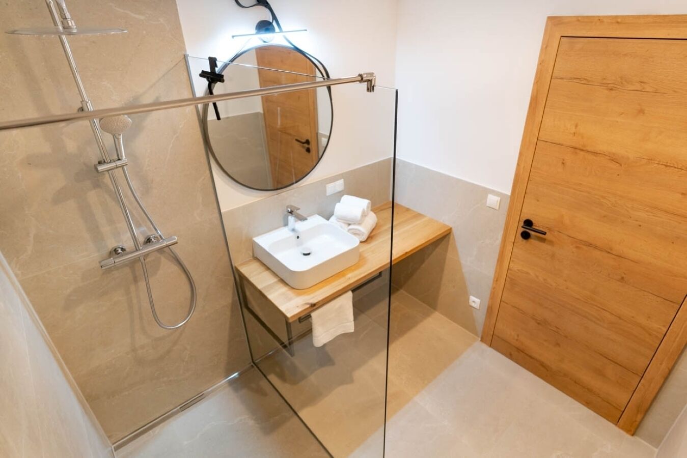 A modern bathroom with a glass-enclosed shower, a wooden vanity with a sink, and a large mirror.