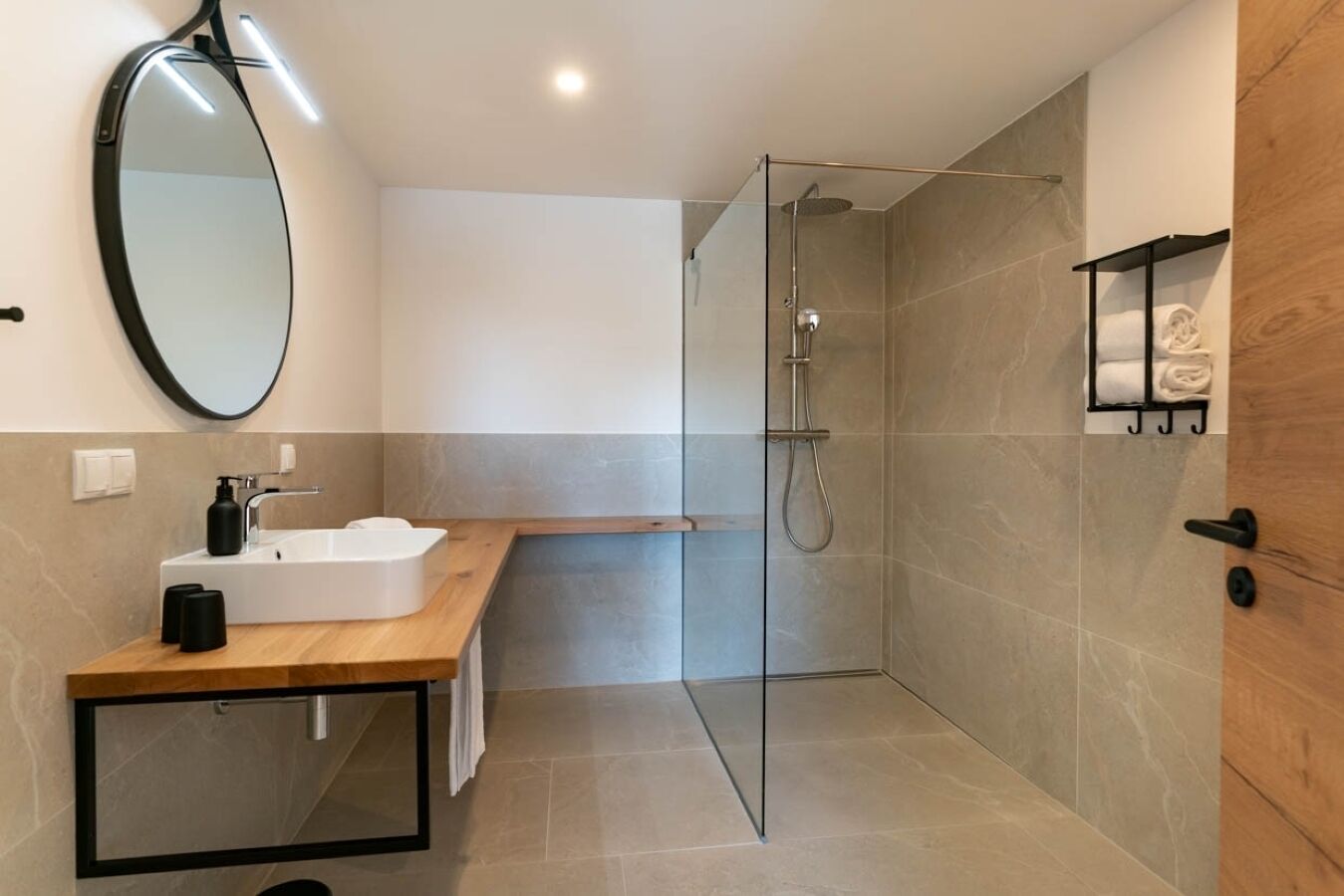A modern bathroom with a glass shower enclosure, a wooden vanity, and a mirror.