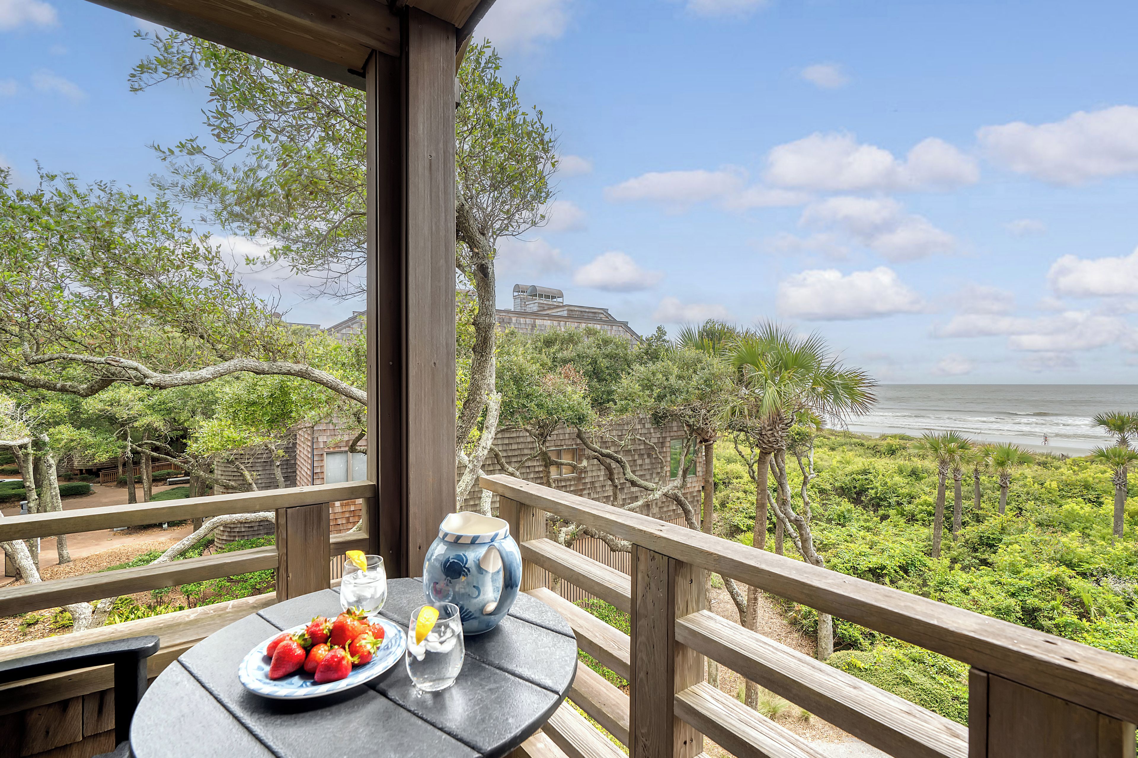 Un balcón con una mesa dispuesta para comer, con vista a una playa y una zona boscosa.