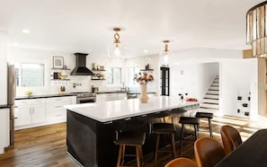 Una cocina moderna con una isla grande, taburetes de bar e iluminación colgante.