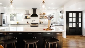 A modern kitchen with a large island, bar stools, pendant lighting, and a black door. - Sunburst Estate - Pool - Hot Tub - Tons of Games! (Scottsdale)