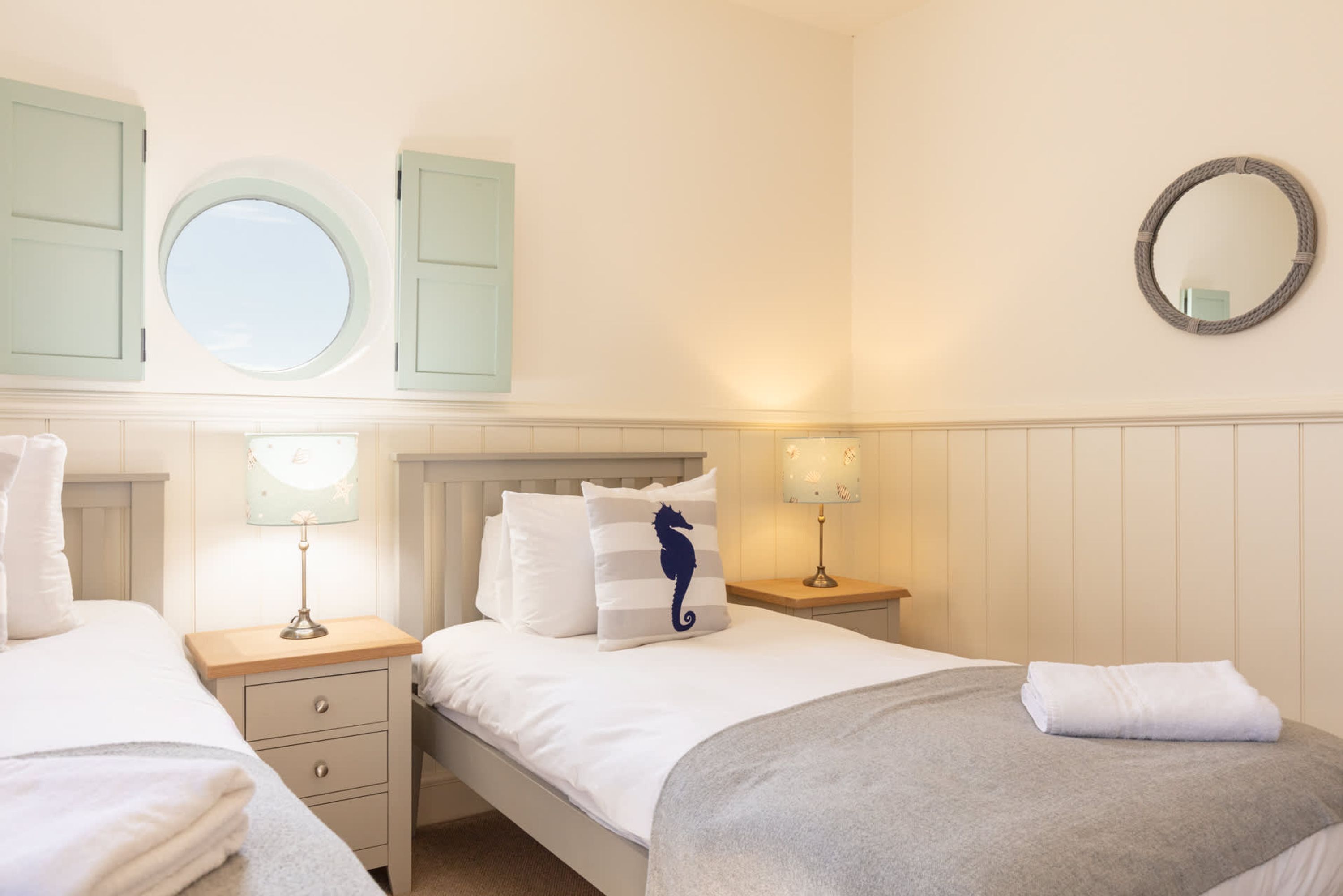 A bedroom with two beds, a window, a mirror, and bedside tables with lamps.