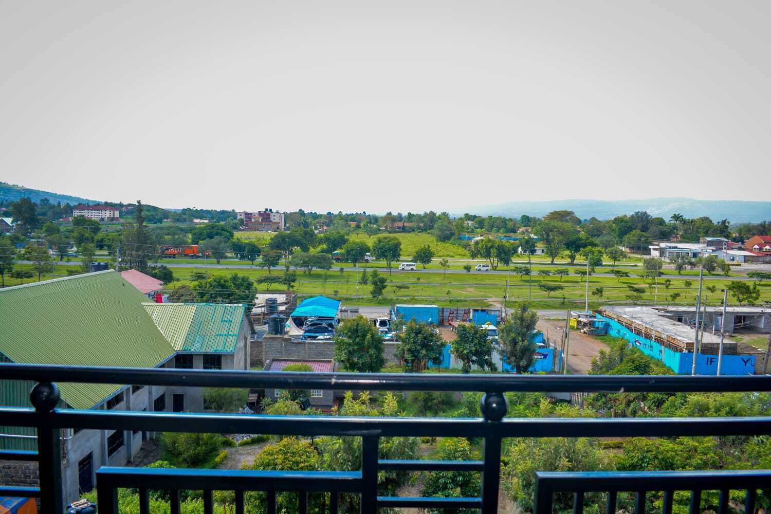 A view from a balcony overlooking a green landscape with buildings, a sports field, and a clear sky.