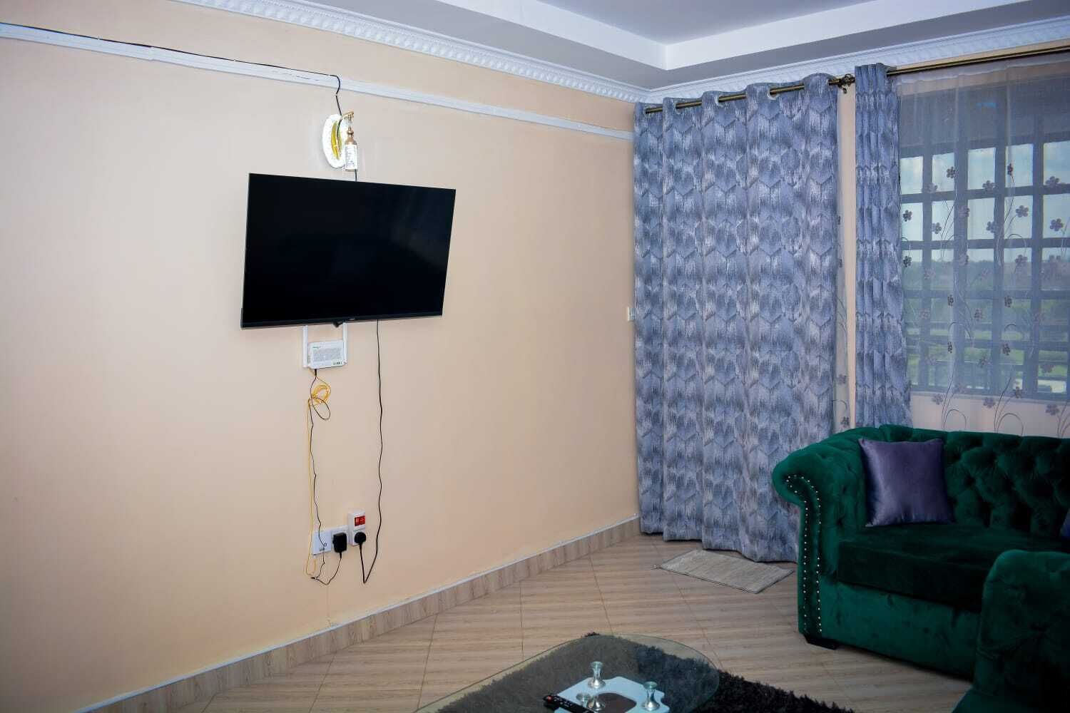Un salon avec un téléviseur à écran plat fixé au mur, un canapé en velours vert et un rideau à motifs.