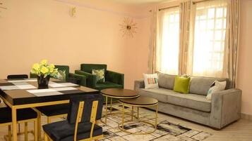 A living room with a sofa, a dining table with chairs, and a decorative clock on the wall.