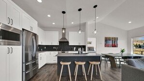 A modern kitchen with white cabinets, stainless steel appliances, a central island with stools, and pendant lighting. - Mountain View Family Retreat w/ Hot Tub & Ski Access (Eden)