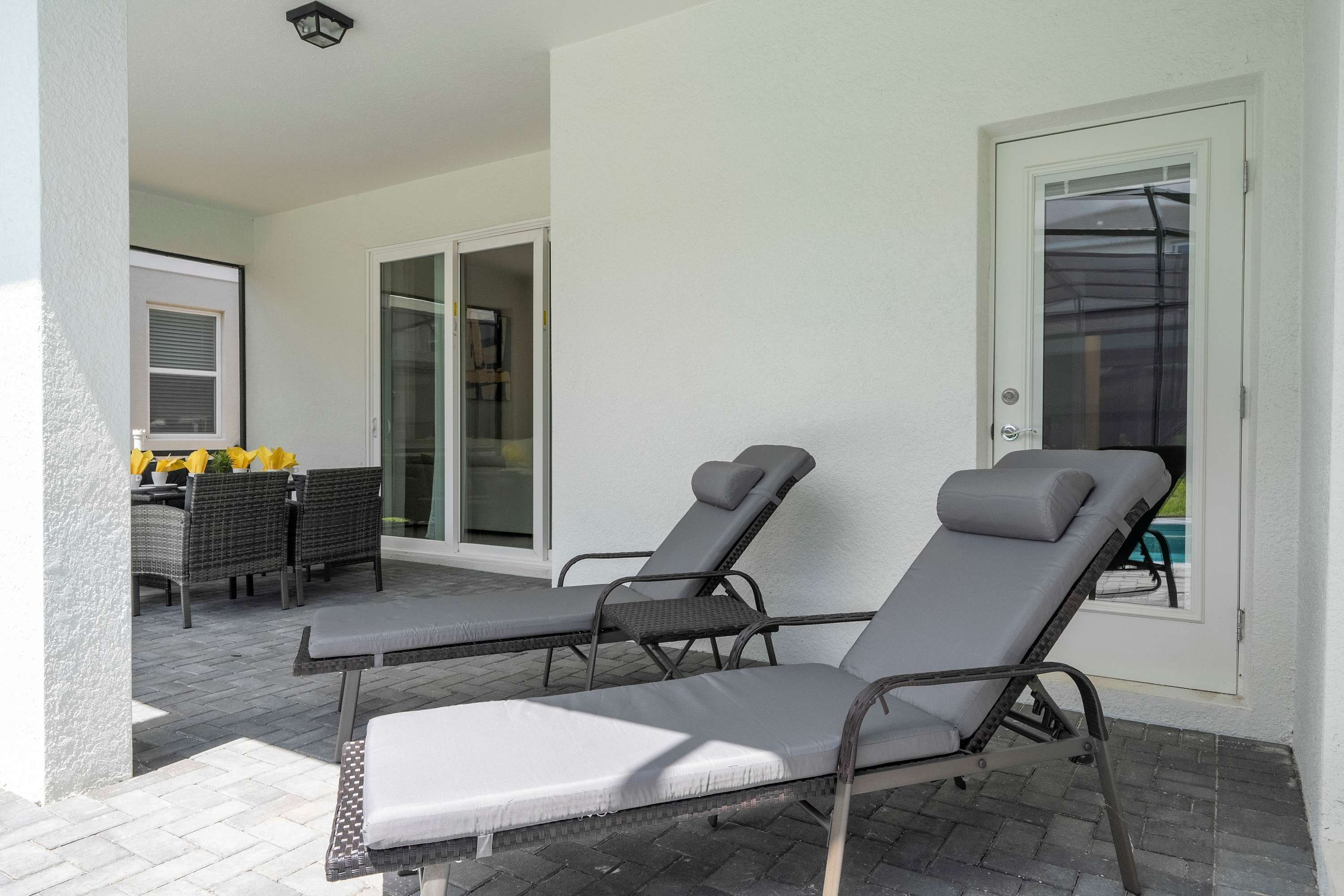 Une terrasse avec deux fauteuils de jardin, une table avec des chaises et une porte-fenêtre coulissante donnant sur une zone abritant une piscine.