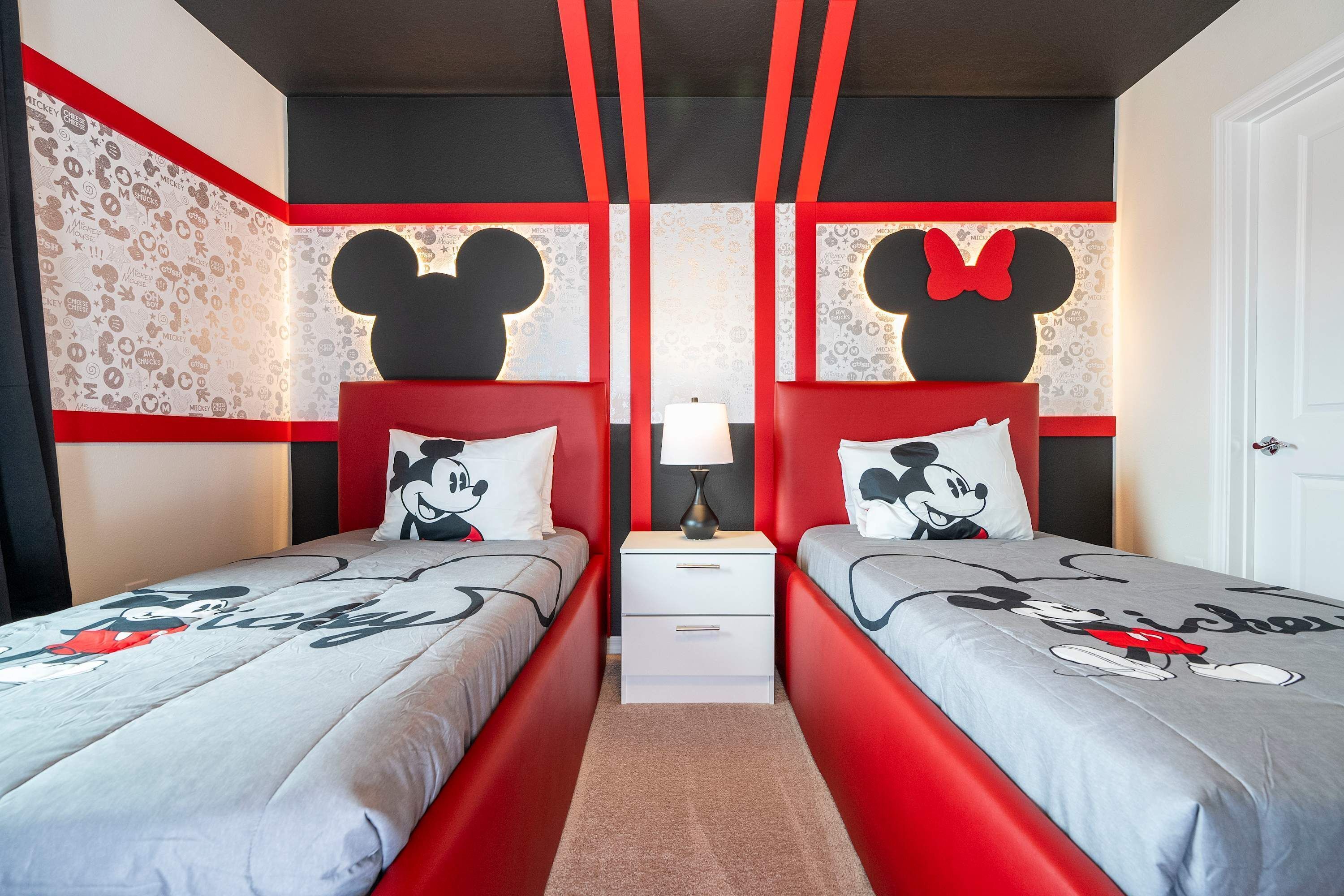 Une chambre avec deux lits, chacun agrémenté de draps et d’oreillers aux motifs de Mickey Mouse. Des tables de chevet avec des lampes sont placées entre les lits.