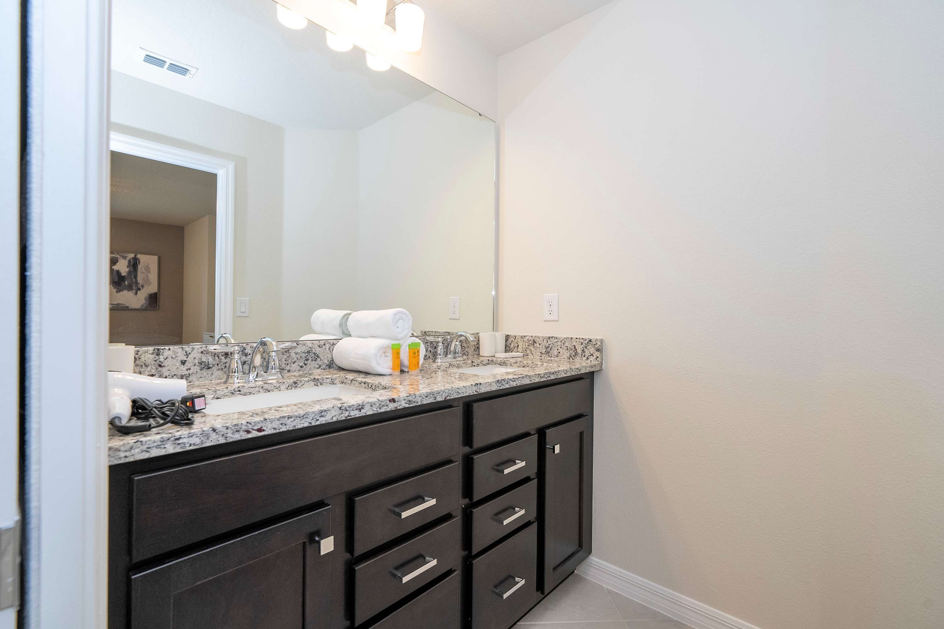 A modern bathroom with a dark vanity, a large mirror, and a granite countertop.