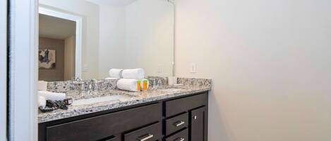 A modern bathroom with a dark vanity, a large mirror, and a granite countertop.