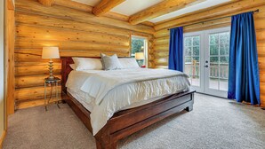 A wooden cabin bedroom with a bed, two bedside lamps, and a view of the outdoors through a door. - Log Cabin w/ Wraparound Deck in Breckenridge! (Breckenridge)