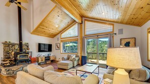 Una sala de estar acogedora con chimenea de piedra, techo de madera, ventanas amplias y asientos cómodos.
