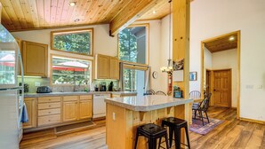 Una cocina amplia con armarios de madera, una isla grande con taburetes y vistas al exterior a través de amplios ventanales.