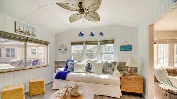 A spacious living room with a white sofa, a round wooden coffee table, wicker ottomans, and a ceiling fan. - Island Cottage in Jensen Beach w/ Pool Access! (Jensen Beach)