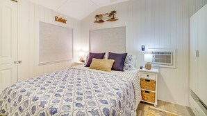 A bedroom with a bed, a nightstand, a wall-mounted air conditioner, and a ceiling fan. - Island Cottage in Jensen Beach w/ Pool Access! (Jensen Beach)