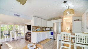A spacious kitchen with white cabinets, a wooden dining table, and a hanging light fixture. - Island Cottage in Jensen Beach w/ Pool Access! (Jensen Beach)