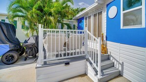 A residential building with a blue exterior, white railings, and a staircase leading to a porch area with wicker furniture. - Island Cottage in Jensen Beach w/ Pool Access! (Jensen Beach)