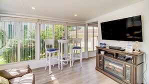A living room with a large TV, a wooden cabinet, and a seating area with two chairs and a sofa. - Island Cottage in Jensen Beach w/ Pool Access! (Jensen Beach)