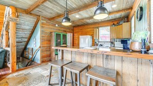 Eine rustikale Küche mit Holzwänden, einer Bar mit Hockern und einem Kühlschrank.