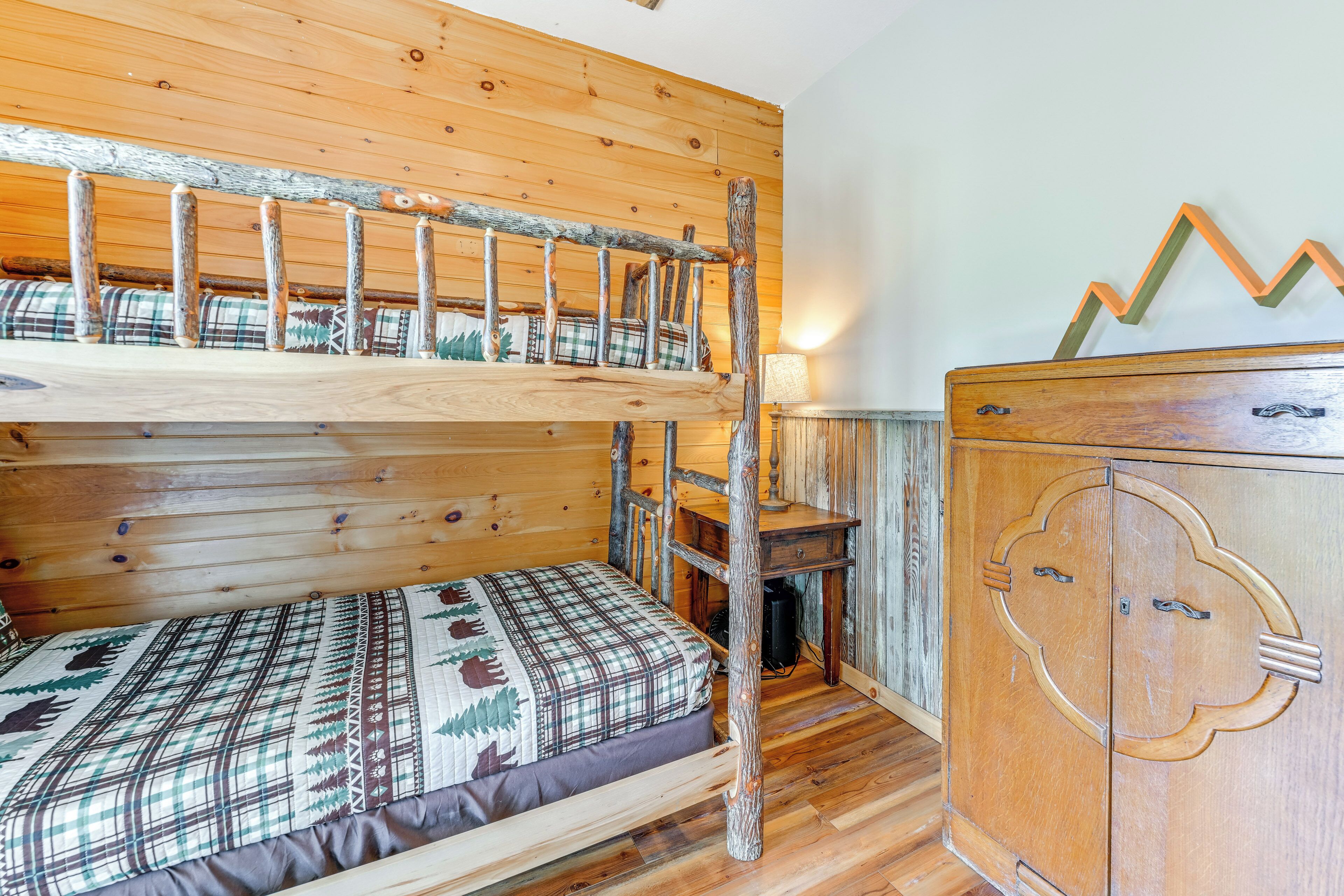 A bunk bed with a plaid bedspread, a wooden dresser with a cloud-shaped drawer, and a wooden headboard.