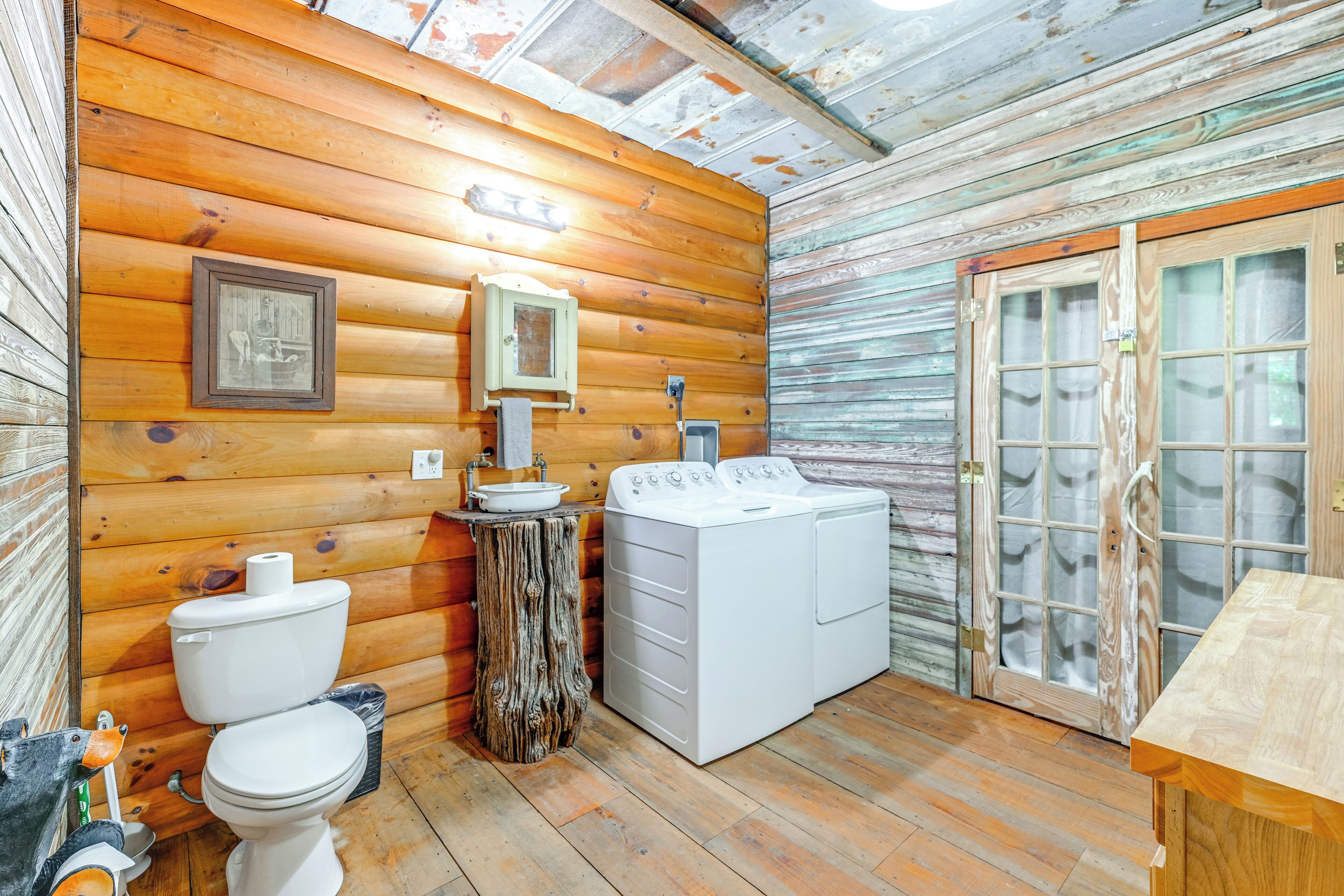 L’intérieur d’un chalet rustique, avec un plancher en bois, des toilettes, un lavabo, un lave-linge et une table en bois.