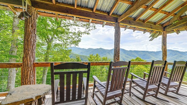 Eine Holzterrasse mit Schaukelstühlen und einem Tisch, mit Blick auf eine gebirgige Landschaft.