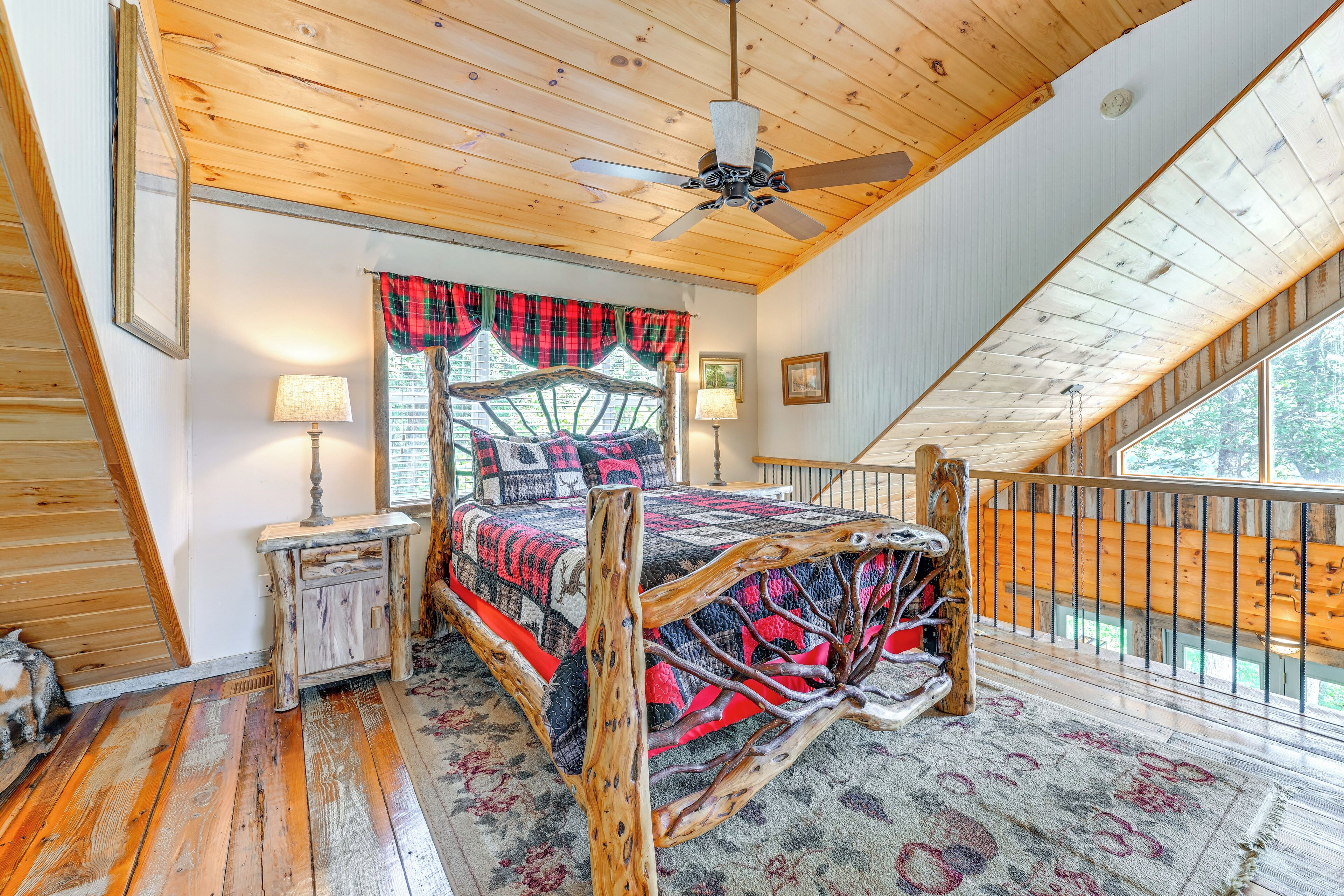 A bedroom with a sloped ceiling, a wooden bed frame, a ceiling fan, and a view of the outdoors.
