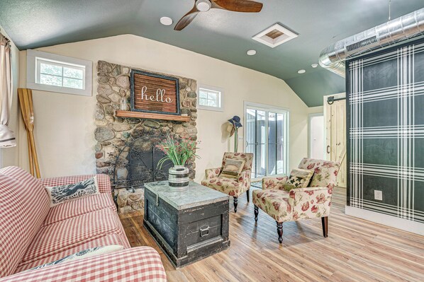A cozy living room with a stone fireplace, a red and white checkered sofa, floral armchairs, and a vintage trunk as a coffee table.