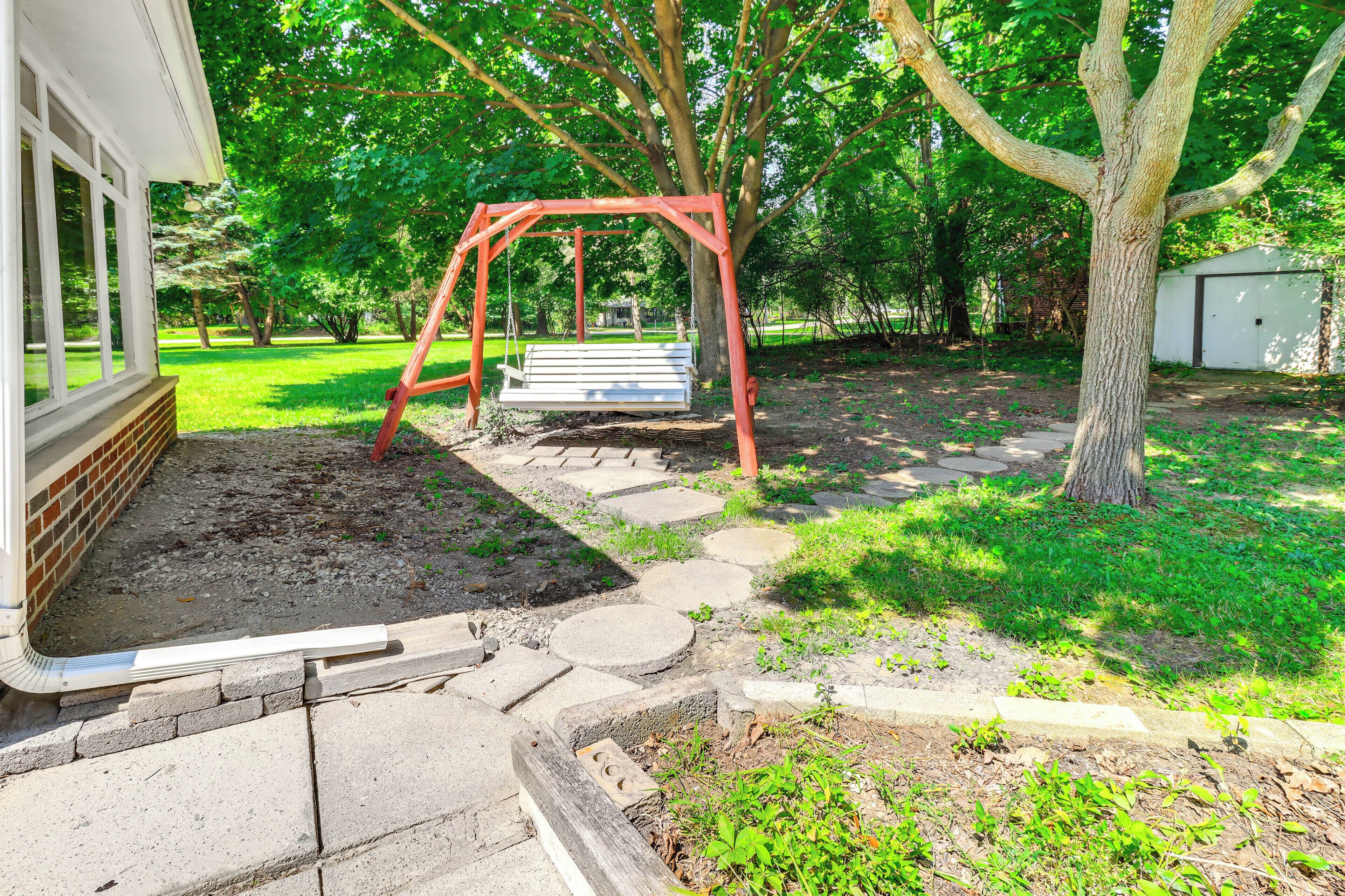 A backyard with a swing set, a brick pathway, and a tree.