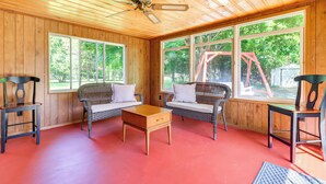 A wooden-paneled room with a red floor, two wicker sofas with white cushions, a wooden coffee table, and a ceiling fan. - Home ~ 17 Mi to Detroit w/ Patio & Grill! (Southfield)