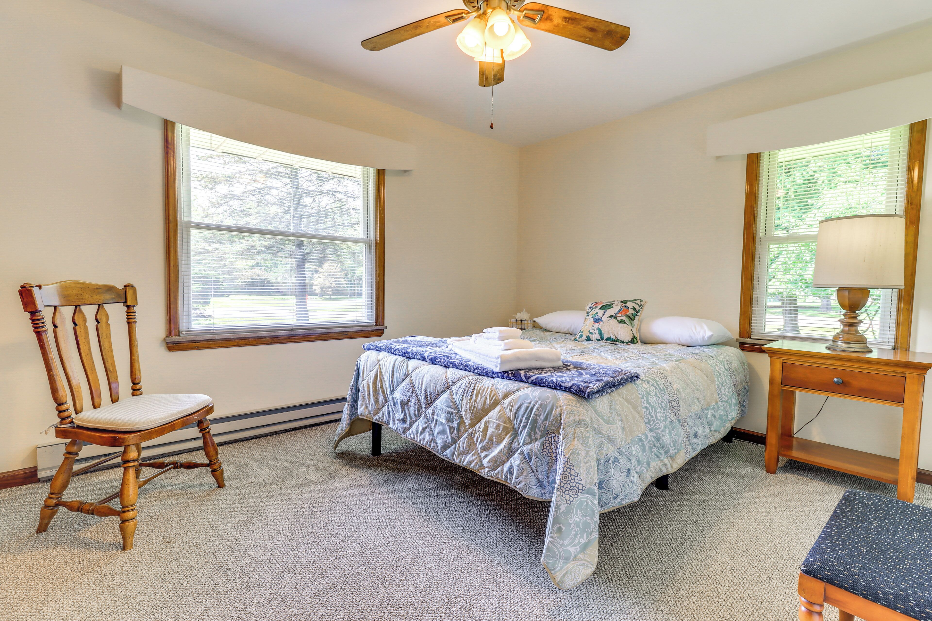 A bedroom with a bed, a wooden chair, a nightstand, a lamp, and a ceiling fan.