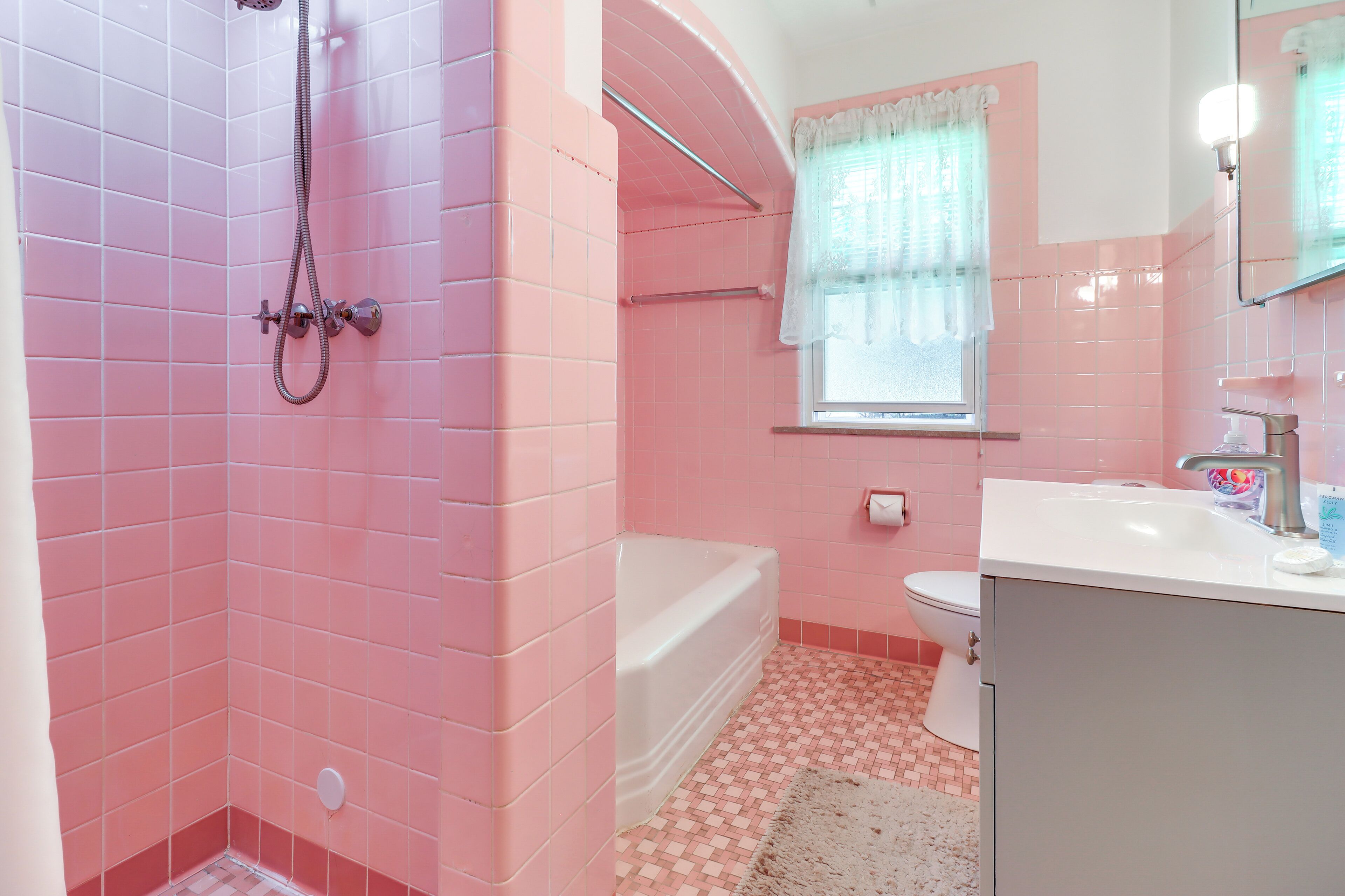A bathroom with pink tiles, a bathtub, a toilet, and a sink.