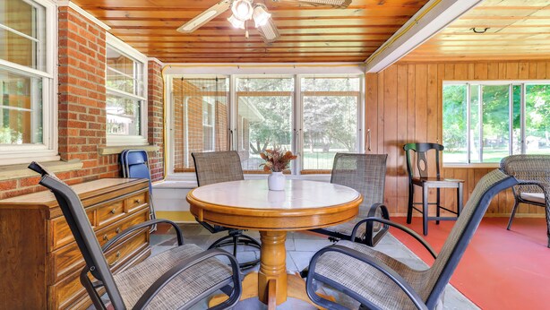 A dining area with a round wooden table and four chairs, a brick wall, and large windows. - Home ~ 17 Mi to Detroit w/ Patio & Grill! (Southfield)