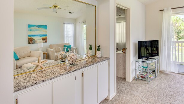 A spacious living room with a large mirror, a television, and a kitchen area with a granite countertop. - Screened Porch & Community Perks: Myrtle Beach Gem (Myrtle Beach)