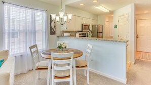 A dining area with a round table, white chairs, a chandelier, and a kitchen in the background. - Screened Porch & Community Perks: Myrtle Beach Gem (Myrtle Beach)