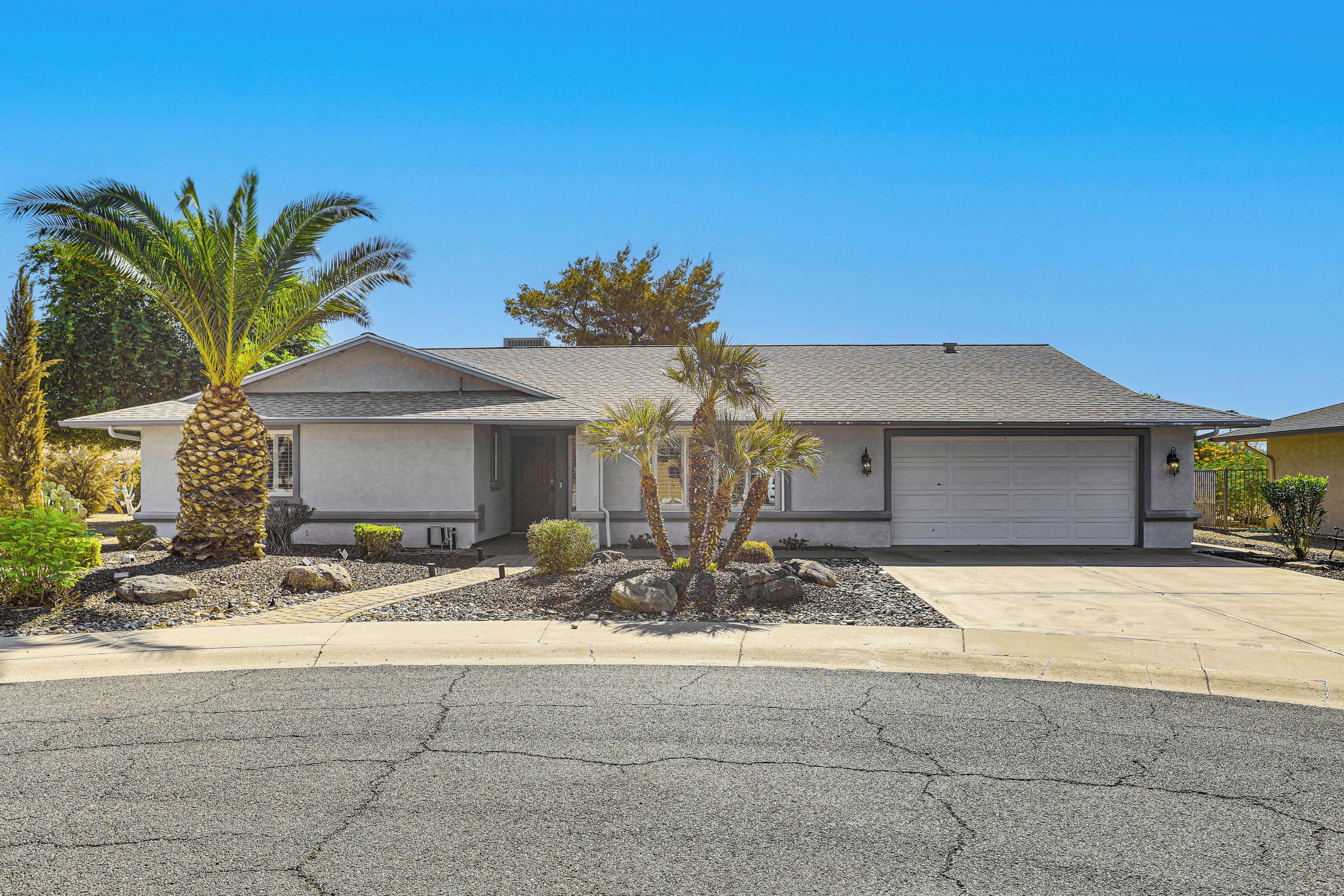 A single-story house with a garage, a driveway, and a landscaped front yard with palm trees and shrubs.